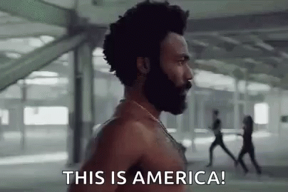 A Shirtless Man With A Beard Is Standing In Front Of A Group Of People . GIF