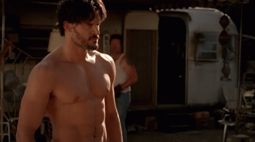 A Shirtless Man With A Beard Is Standing In Front Of A Trailer In A Dark Room . GIF