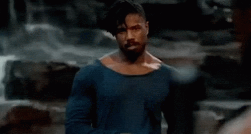 A Shirtless Man With A Beard Is Standing In Front Of A Waterfall In A Cave . GIF
