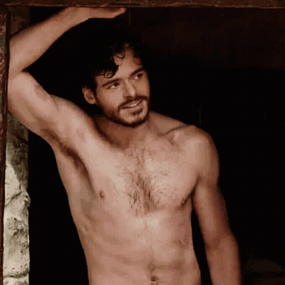 A Shirtless Man With A Beard Is Standing Next To A Window . GIF