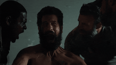 A Shirtless Man With A Beard Is Surrounded By Two Men GIF