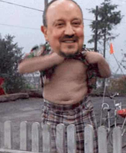 A Shirtless Man With A Big Head Is Standing Behind A Fence GIF