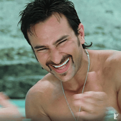 A Shirtless Man With A Chain Around His Neck Smiles For The Camera GIF