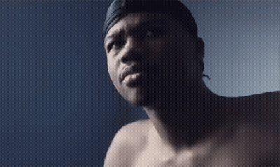 A Shirtless Man With A Headband On His Head Looks At The Camera . GIF