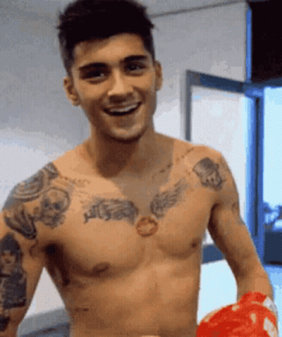 A Shirtless Man With A Lot Of Tattoos On His Chest Is Holding A Red Boxing Glove . GIF
