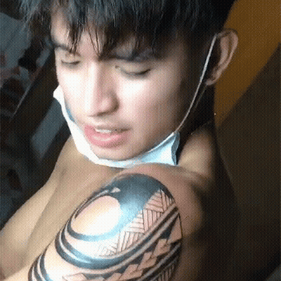 A Shirtless Man With A Mask On His Face Is Getting A Tattoo On His Arm . GIF