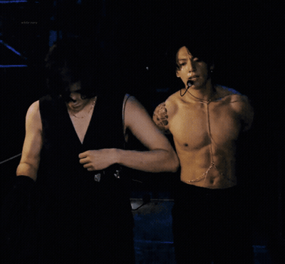 A Shirtless Man With A Microphone Around His Neck Looks At The Camera GIF