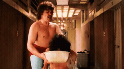 A Shirtless Man With A Mustache Is Holding A Bowl Of Water Over A Woman 'S Head GIF