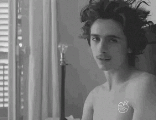 A Shirtless Man With A Sticker On His Chest Is Sitting On A Bed . GIF