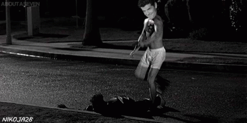 A Shirtless Man With A Tattoo Of A Star On His Chest Is Standing On The Sidewalk . GIF