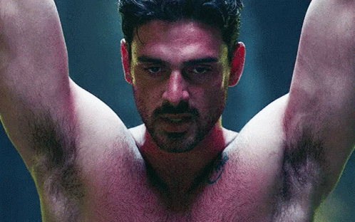 A Shirtless Man With A Tattoo On His Arm Is Hanging Upside Down With His Arms Outstretched . GIF