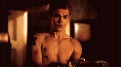 A Shirtless Man With A Tattoo On His Arm Is Standing In A Room . GIF