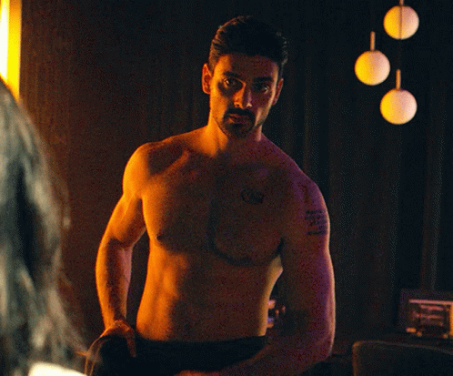 A Shirtless Man With A Tattoo On His Arm Is Standing In Front Of A Mirror GIF