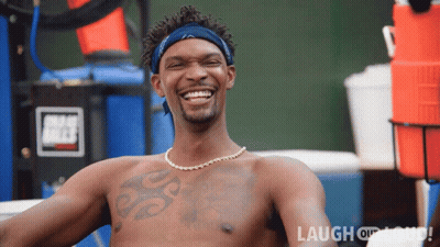 A Shirtless Man With A Tattoo On His Chest Is Smiling In Front Of A Sign That Says Laugh Or Die GIF