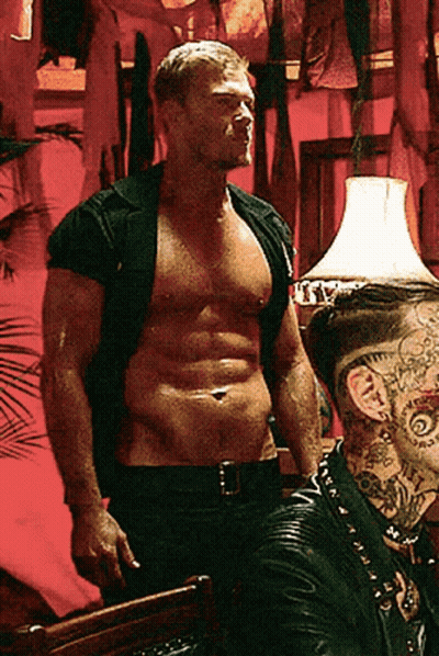 A Shirtless Man With A Tattoo On His Neck Stands Next To Another Man GIF