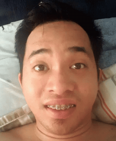 A Shirtless Man With Braces On His Teeth Is Laying On A Bed GIF