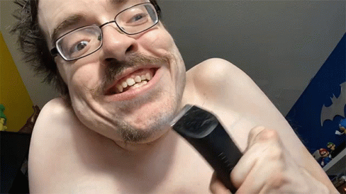A Shirtless Man With Glasses And A Mustache Is Smiling While Holding A Clipper GIF