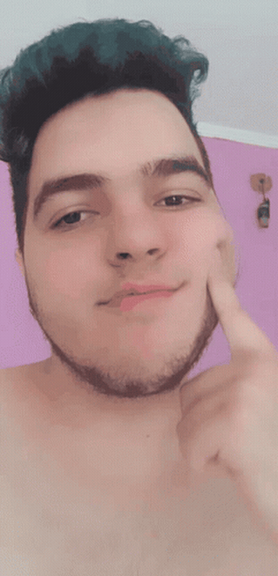A Shirtless Man With Green Hair And A Beard Touches His Face With His Finger GIF