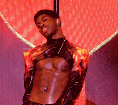 A Shirtless Man With His Tongue Hanging Out Stands In Front Of A Red Heart GIF