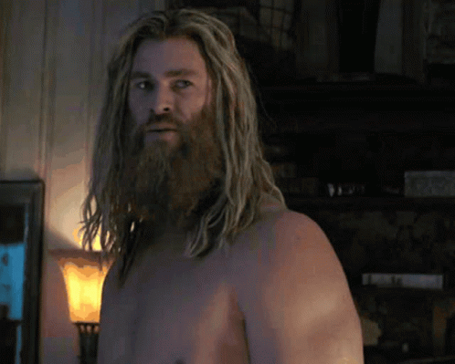 A Shirtless Man With Long Hair And A Beard Is Standing In A Living Room . GIF