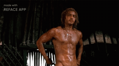 A Shirtless Man With Long Hair Is Standing In Front Of A Fence In A Dark Room . GIF