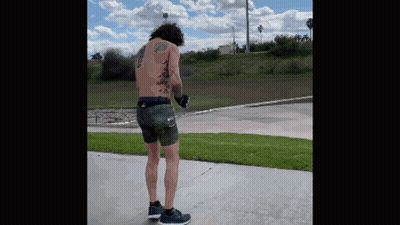 A Shirtless Man With Tattoos On His Back Is Standing On A Sidewalk . GIF