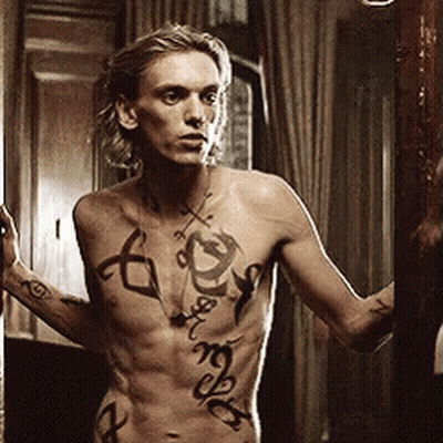 A Shirtless Man With Tattoos On His Chest Is Looking At Himself In A Mirror GIF
