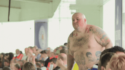 A Shirtless Man With Tattoos On His Chest Stands In Front Of A Crowd Of People GIF