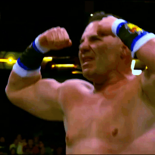 A Shirtless Wrestler Flexes His Muscles In Front Of A Crowd With The Letter L Visible In The Background GIF