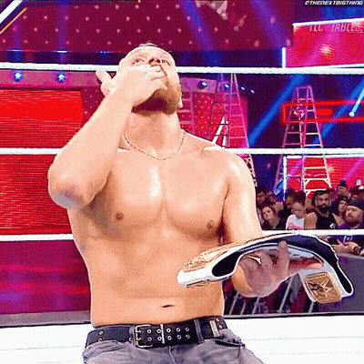 A Shirtless Wrestler Is Holding A Championship Belt In A Ring GIF