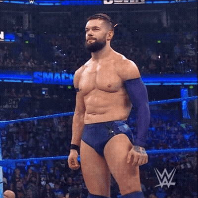 A Shirtless Wrestler Is Standing In A Wrestling Ring With A Smack Down Sign Behind Him GIF