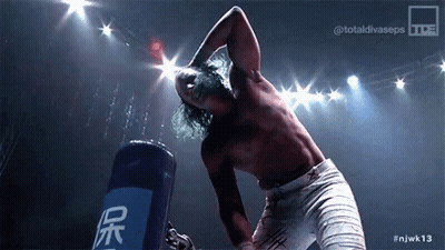 A Shirtless Wrestler Is Standing In Front Of A Blue Bag That Says ' Njwk13 ' On It GIF