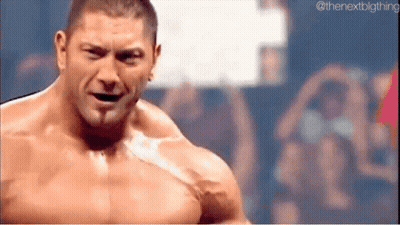 A Shirtless Wrestler Is Standing In Front Of A Crowd And Looking At The Camera . GIF