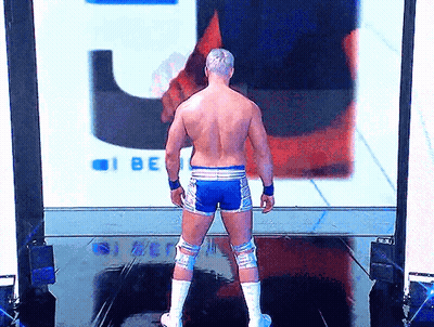 A Shirtless Wrestler Is Standing In Front Of A Large Screen That Says I Be GIF