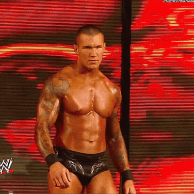 A Shirtless Wrestler Is Standing In Front Of A Large Screen With A W Logo On It GIF