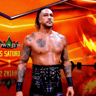 A Shirtless Wrestler Is Standing In Front Of A Sign That Says Crown Jewel Saturday GIF