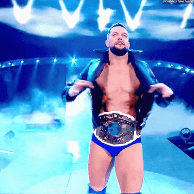 A Shirtless Wrestler Is Standing On A Stage With A Belt Around His Waist .. GIF
