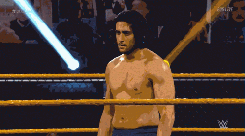 A Shirtless Wrestler Stands In A Wrestling Ring With A Referee Behind Him And 205 Live Written On The Bottom GIF
