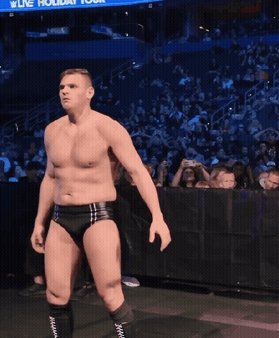 A Shirtless Wrestler Stands In Front Of A Crowd With A Sign That Says Live Holiday Tour GIF