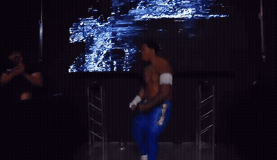 A Shirtless Wrestler Stands In Front Of A Large Screen That Says Zilla GIF