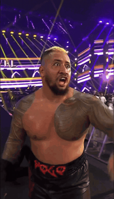 A Shirtless Wrestler Wearing A Belt With The Letter G On It Stands On A Stage GIF