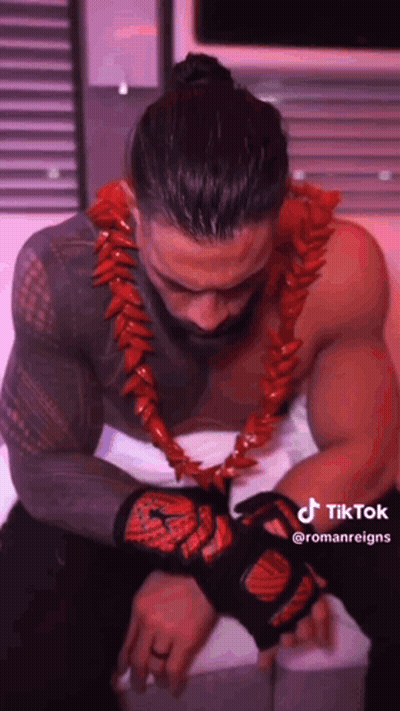 A Shirtless Wrestler Wearing A Red Lei And Gloves Is Sitting On A Bed . GIF