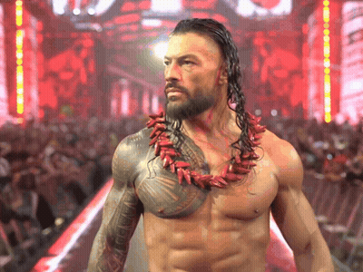 A Shirtless Wrestler Wearing A Red Necklace Stands In Front Of A Crowd Of People GIF