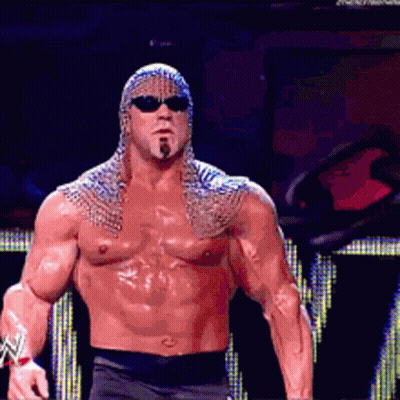 A Shirtless Wrestler Wearing Sunglasses And A Chain Mail Cape GIF