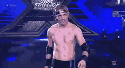 A Shirtless Wrestler With A Bandana On His Head Stands In Front Of A Blue Background GIF