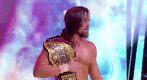 A Shirtless Wrestler With A Beard Is Holding A Championship Belt . GIF
