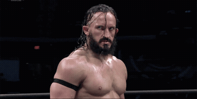 A Shirtless Wrestler With A Beard Stands In A Ring With A Black Band Around His Arm GIF