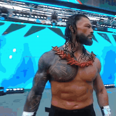 A Shirtless Wrestler With A Necklace Around His Neck Stands In Front Of A Large Screen GIF