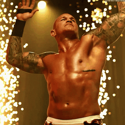 A Shirtless Wrestler With A Tattoo On His Chest Stands In Front Of Sparks GIF