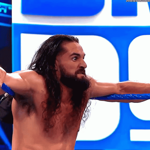 A Shirtless Wrestler With Long Hair And A Beard Is Standing In Front Of A Blue Sign With The Letter D On It GIF